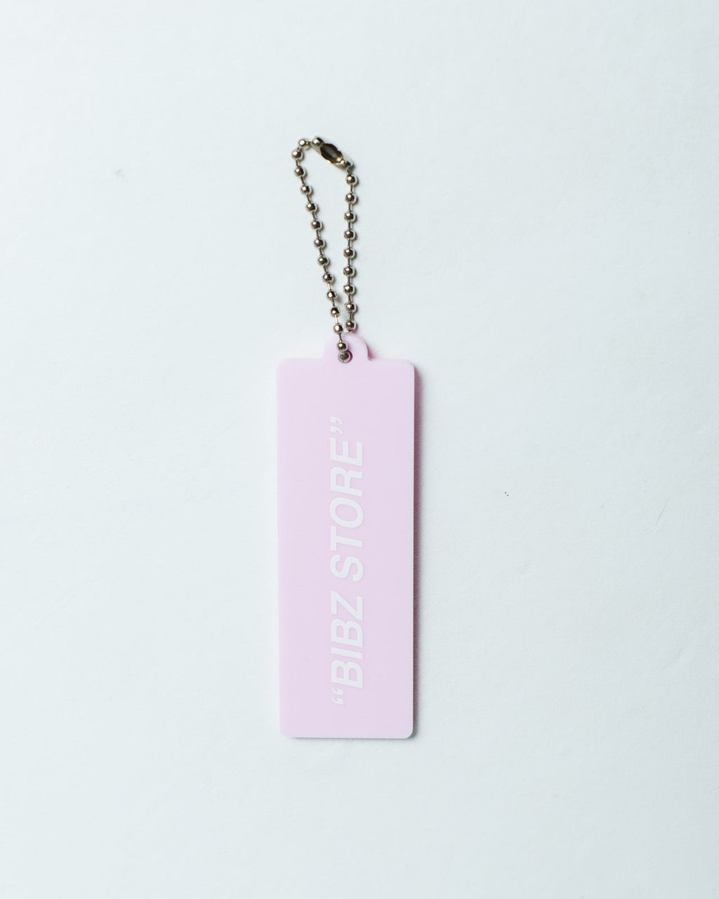 A light pink rectangular keychain tag with the text "BIBZ STORE" printed vertically in white, attached to a silver ball chain, on a plain white background.