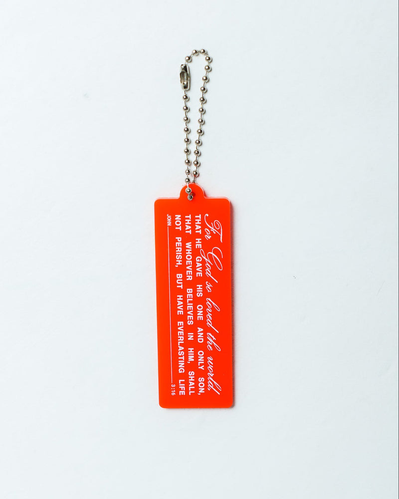 A bright red rectangular acrylic keychain tag featuring white printed text  with the Bible verse John 3:16 and script, attached to a silver ball chain, shown against a plain white background.