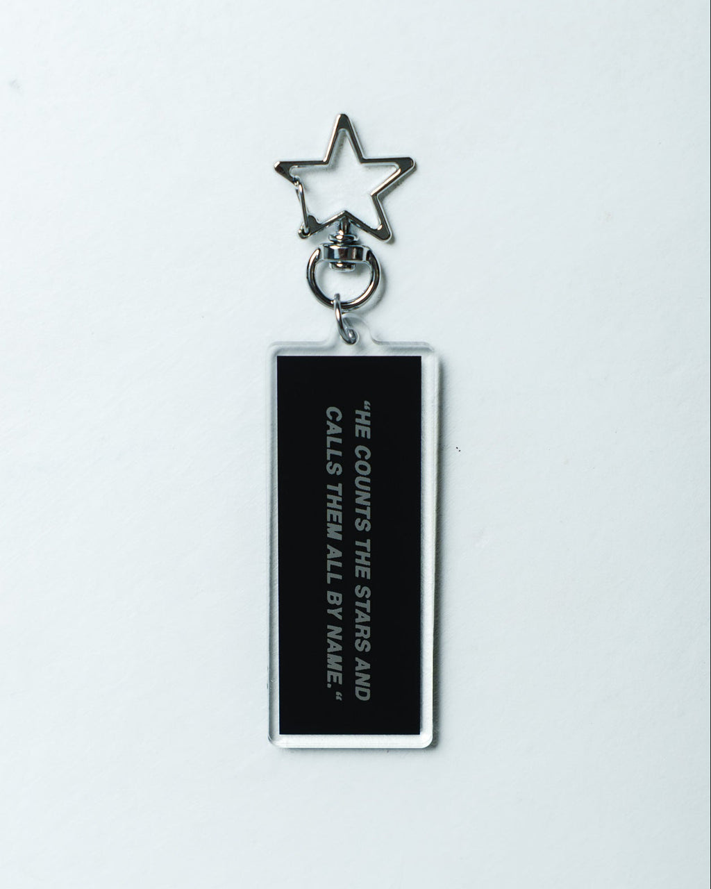 A black rectangular acrylic keychain with white text reading 'HE COUNTS THE STARS AND CALLS THEM ALL BY NAME' and a silver metal star keyring, shown on a plain white background.