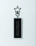 A black rectangular acrylic keychain with white text reading 'HE COUNTS THE STARS AND CALLS THEM ALL BY NAME' and a silver metal star keyring, shown on a plain white background.