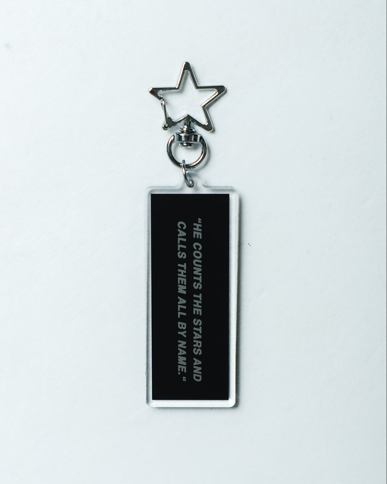 A black rectangular acrylic keychain with white text reading 'HE COUNTS THE STARS AND CALLS THEM ALL BY NAME' and a silver metal star keyring, shown on a plain white background.