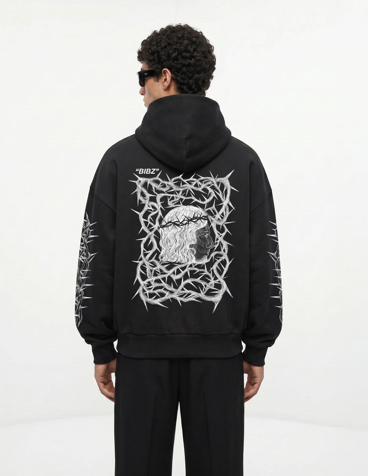 Person wearing a black hoodie with a white graphic design on the back, standing against a white background.